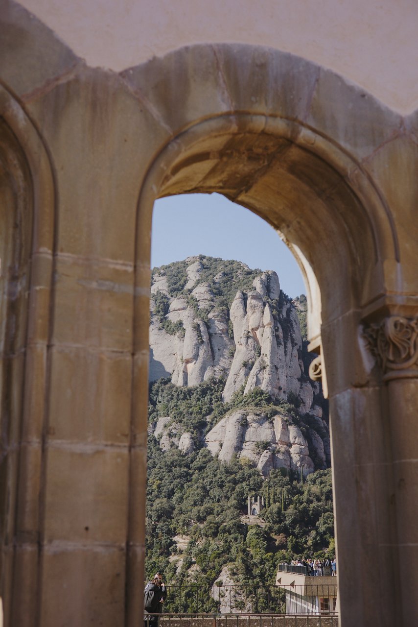 Stone arches overlooking the mountains from a viewpoint, with clear light and strong shadows on the ground.