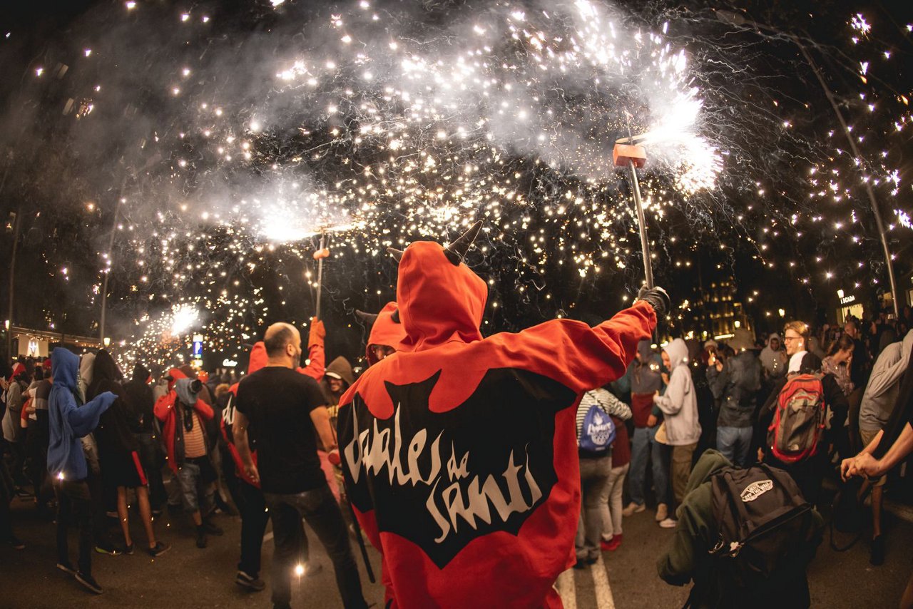 Correfoc participant dressed in red, surrounded by people and flying sparks.