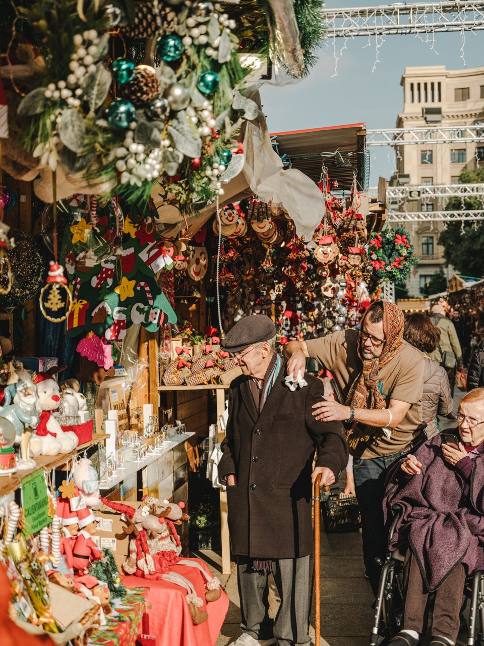 Bancarella di mercato natalizio piena di decorazioni e statuine, con persone che passeggiano e osservano i prodotti in un’atmosfera festosa all’aperto.