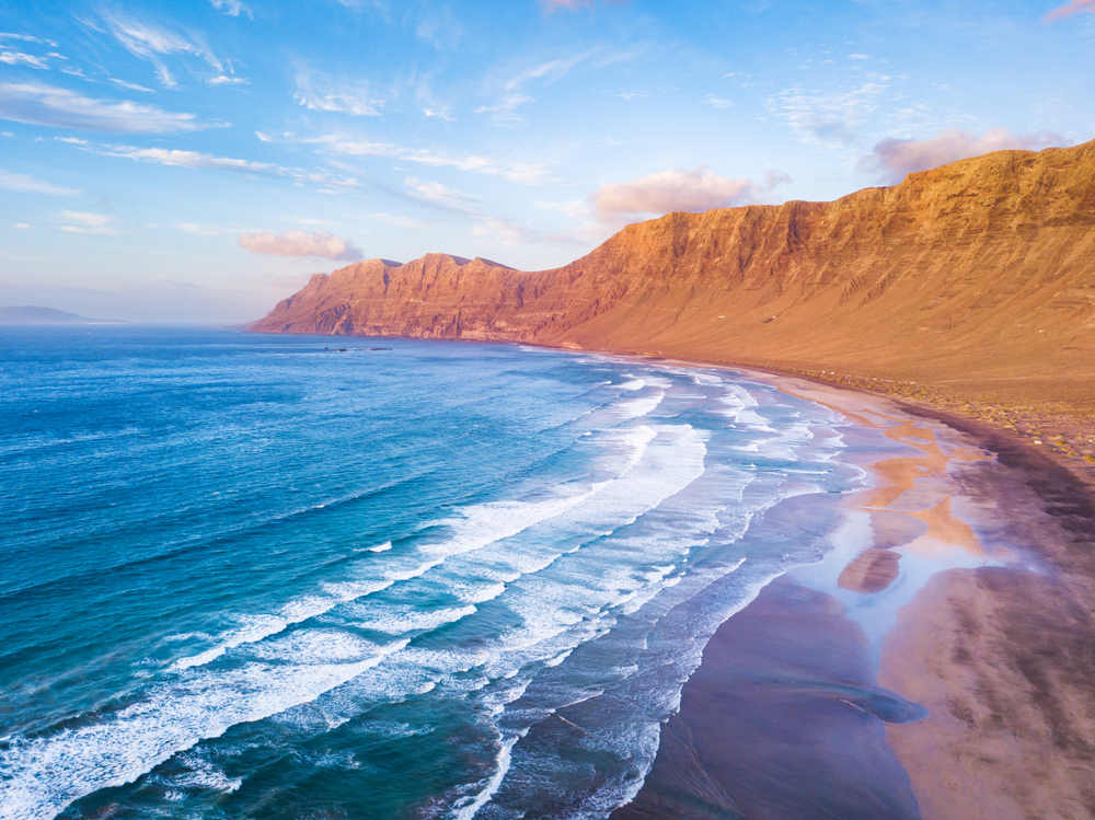 Things to do in Lanzarote: The sun shining on the red cliffs of Famara Beach