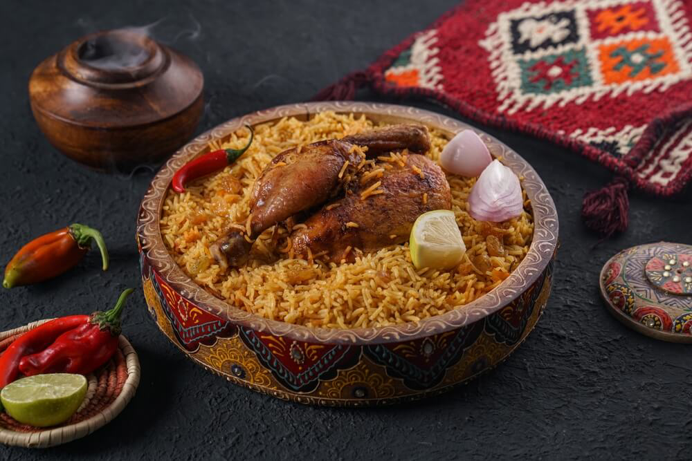 Bunte Schüssel mit Kabsa auf dekoriertem Tisch.