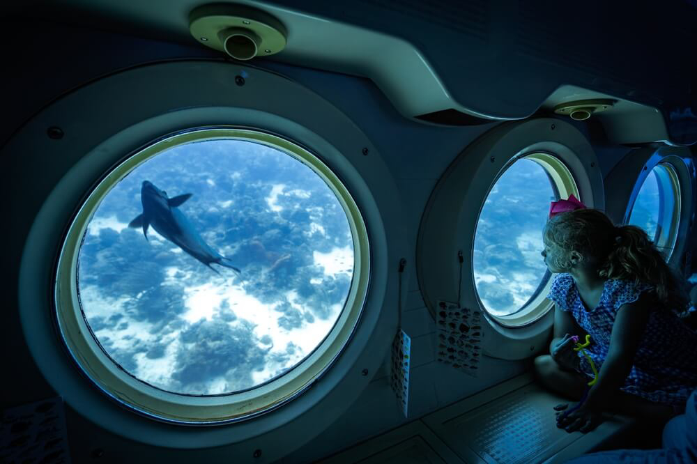 A young girl looks out a submarine window on her Aruba family vacation.