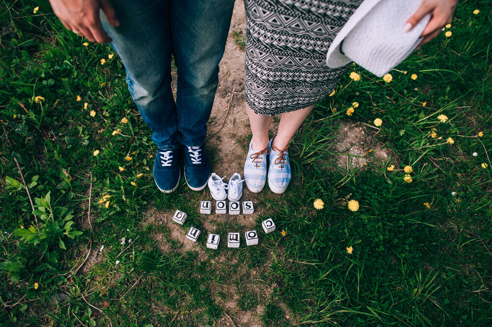 Babymoon: Füße von werdenden Eltern mit Babyschühchen und "coming soon"