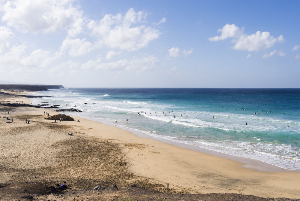 White sand with volcanic rocks along the bay and topaz waves