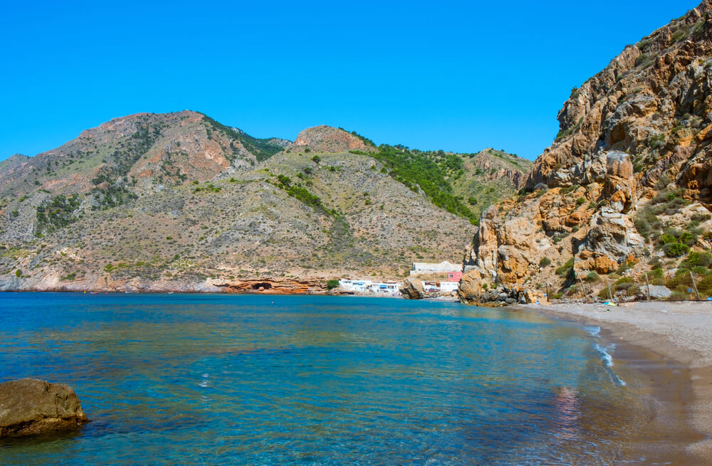 Unberührter Strand mit blauem Wasser, von Bergen umgeben, in der Sierra de la Muela.