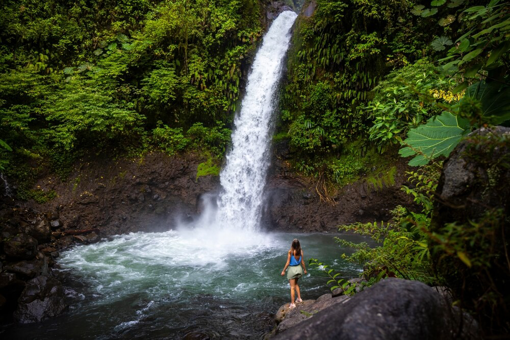 Costa Rica mit Kindern: Mädchen steht vor einem großen Wasserfall.