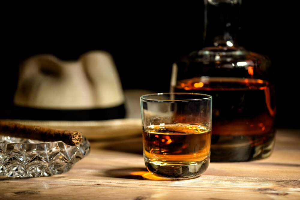 Learn about rum: A rum glass, filled with rum on a table next to a cigar