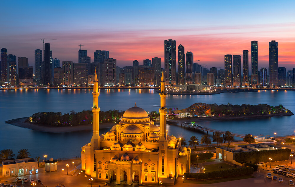 Nächtlicher Blick auf Moschee, Lagune und Hochhäuser im Emirat Sharjah.