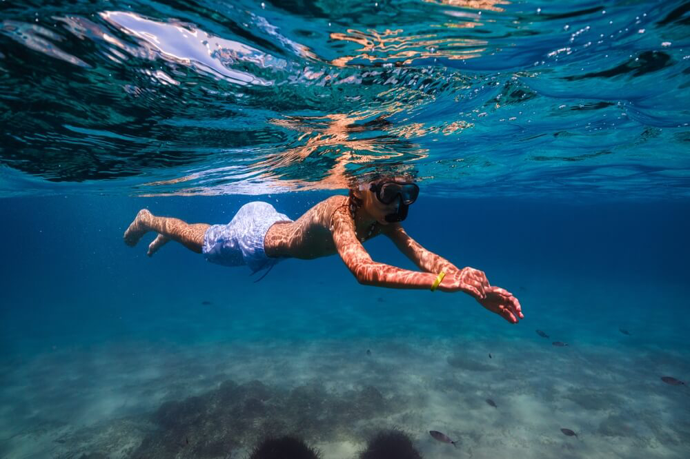 Family resorts: Boy snorkelling in the ocean in light blue swim trunks