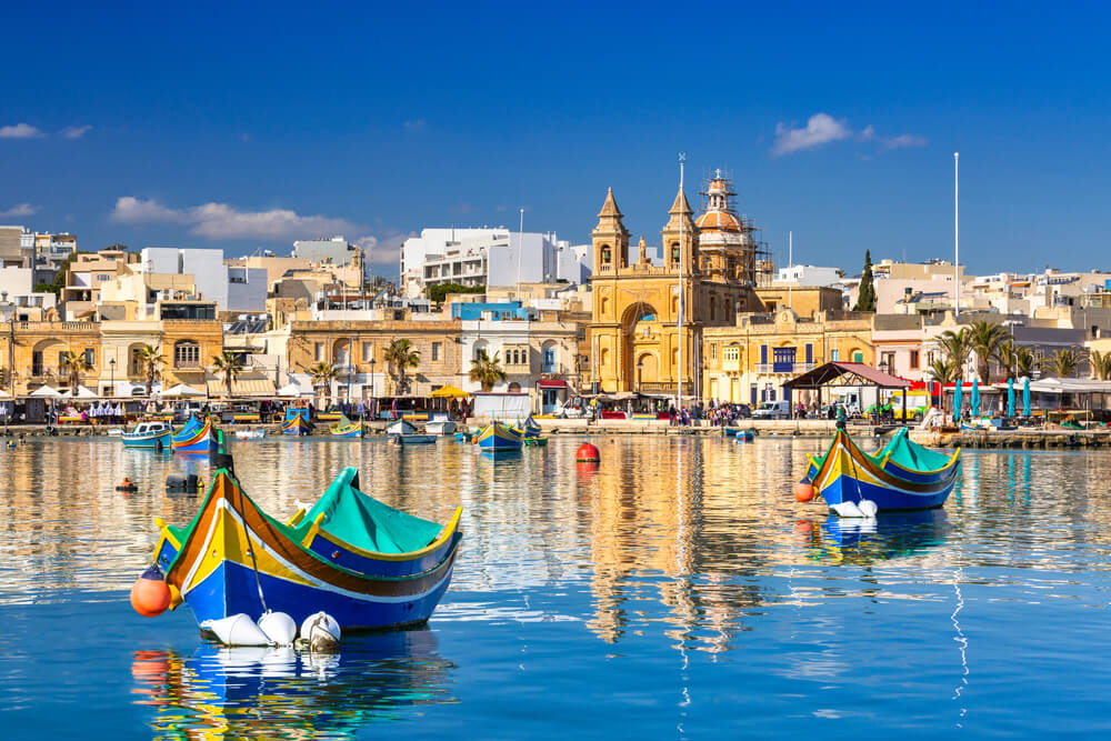 Blick vom Wasser aus auf den Ort Marsaxlokk mit pittoresken Fischerbooten.