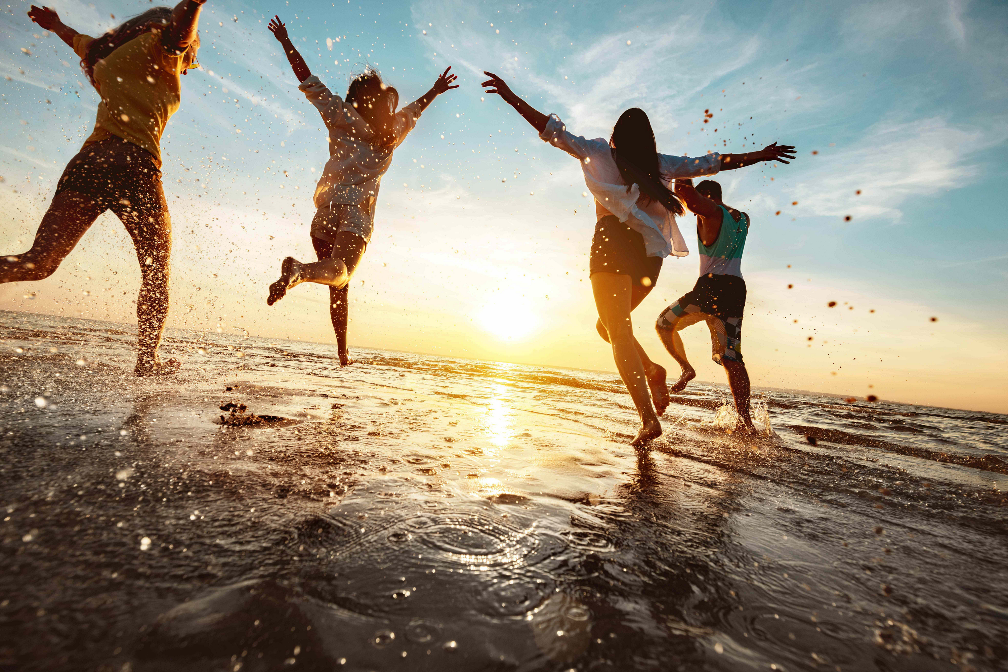 Group of friends jumping through the sea at sunset