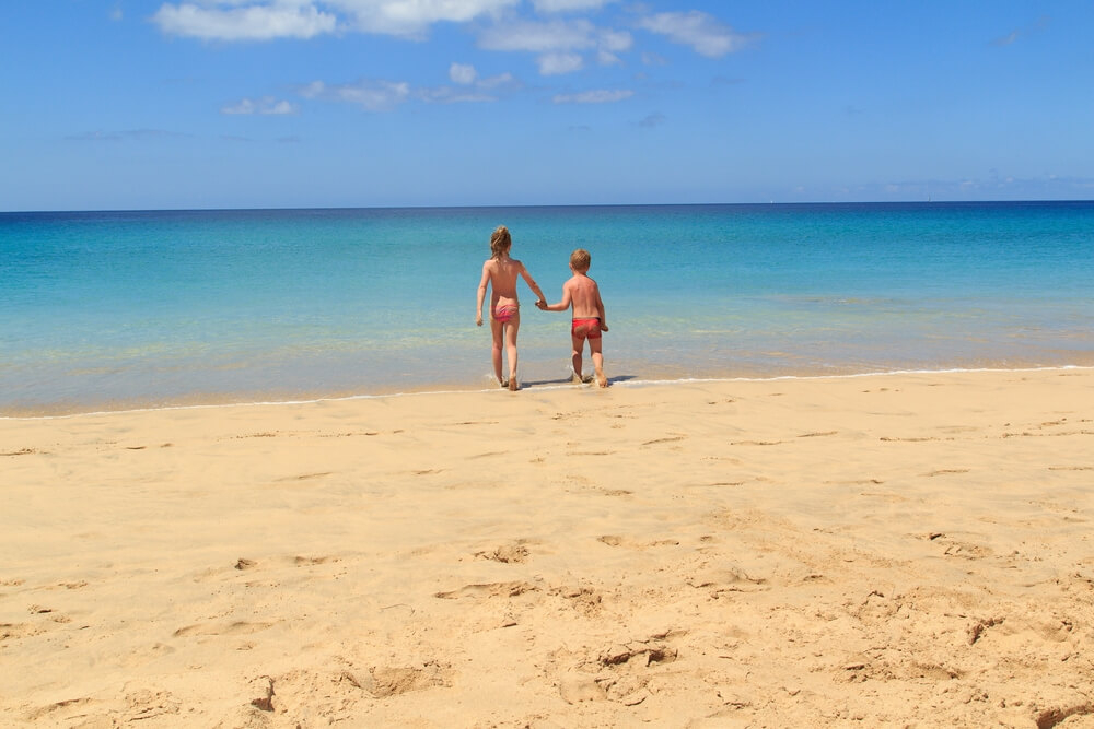 Fuerteventura family holidays: Two toddlers, a boy and a girl holding hands on the beach