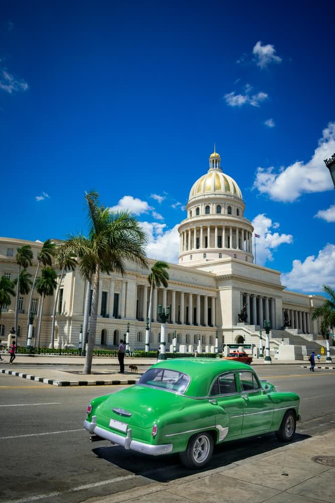 Hemingway Cuba: A street view of a typical main street with a state building and green car