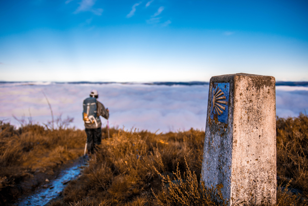 Man hiking the Camino de Santiago with close-up of a scallop shell sign