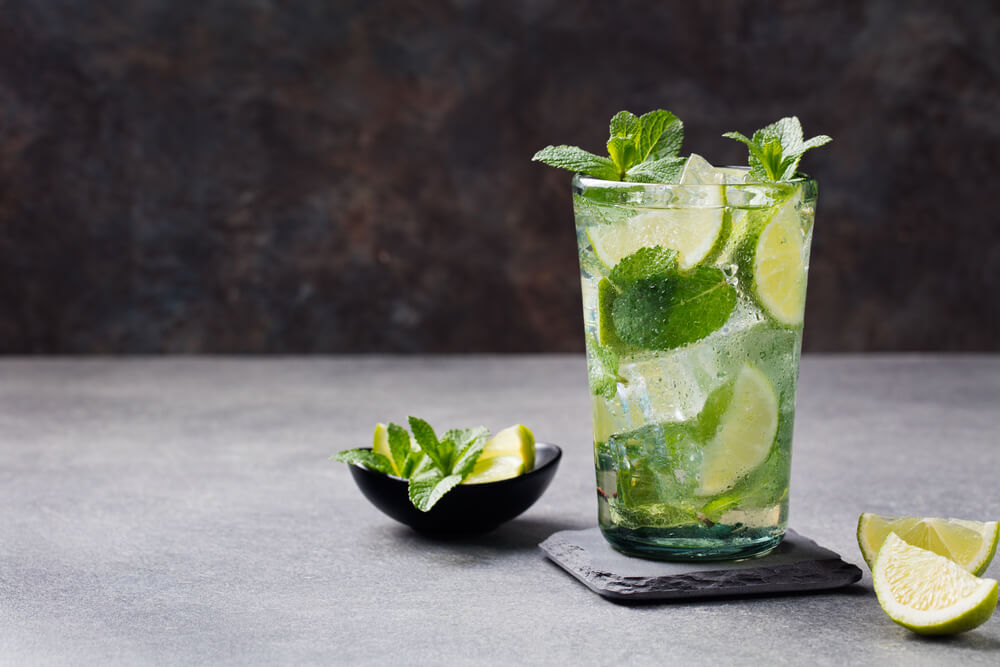 Karibische Cocktails: Mojito-Glas mit Limettenstücken und Minze.