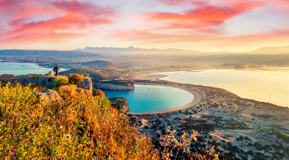 Voidokilia Beach: Sun setting across the bay of the beach with a man taking a photo 