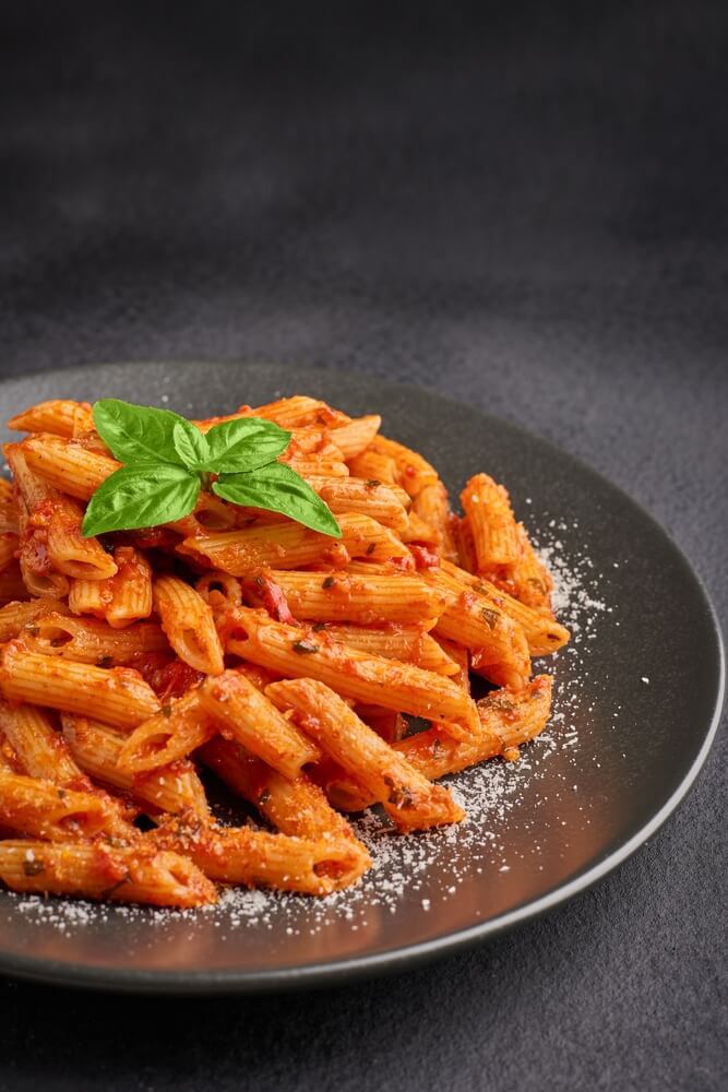 Roman cuisine: A plate of penne all’arrabbiata on a dark plate and background