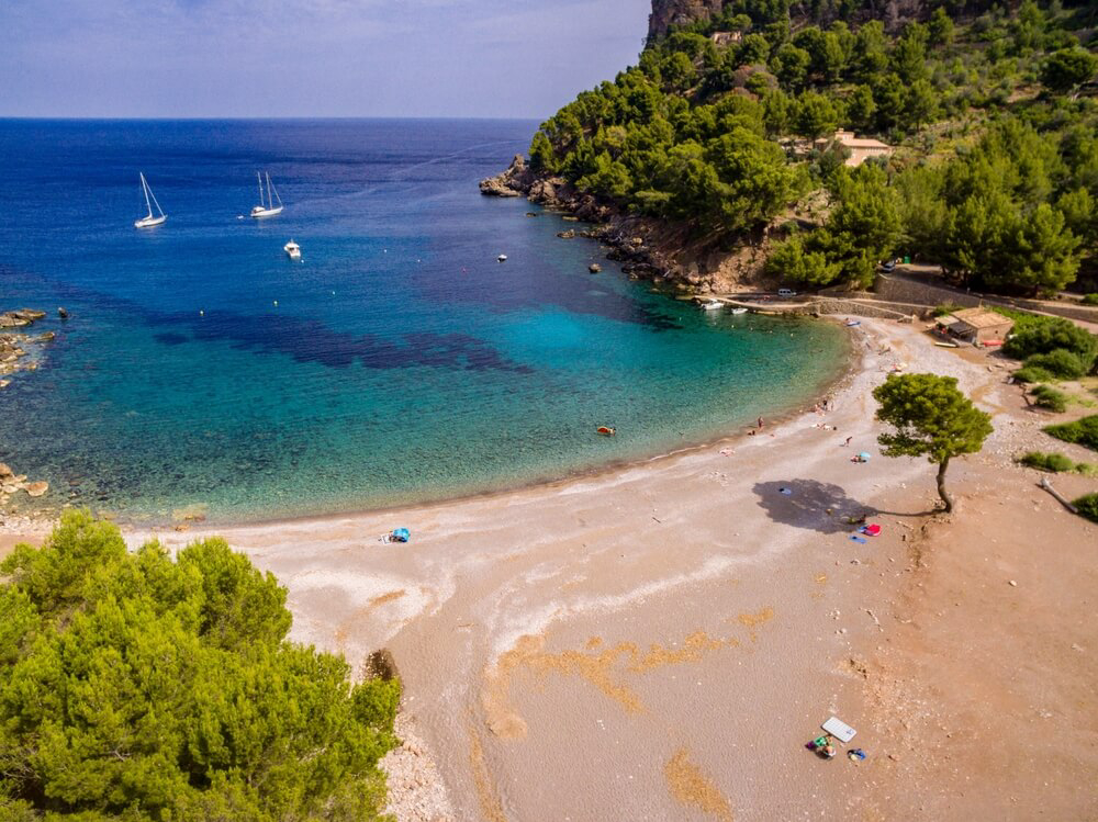 Die Cala Tuent auf Mallorca, umgeben von Felsen mit Pinien.