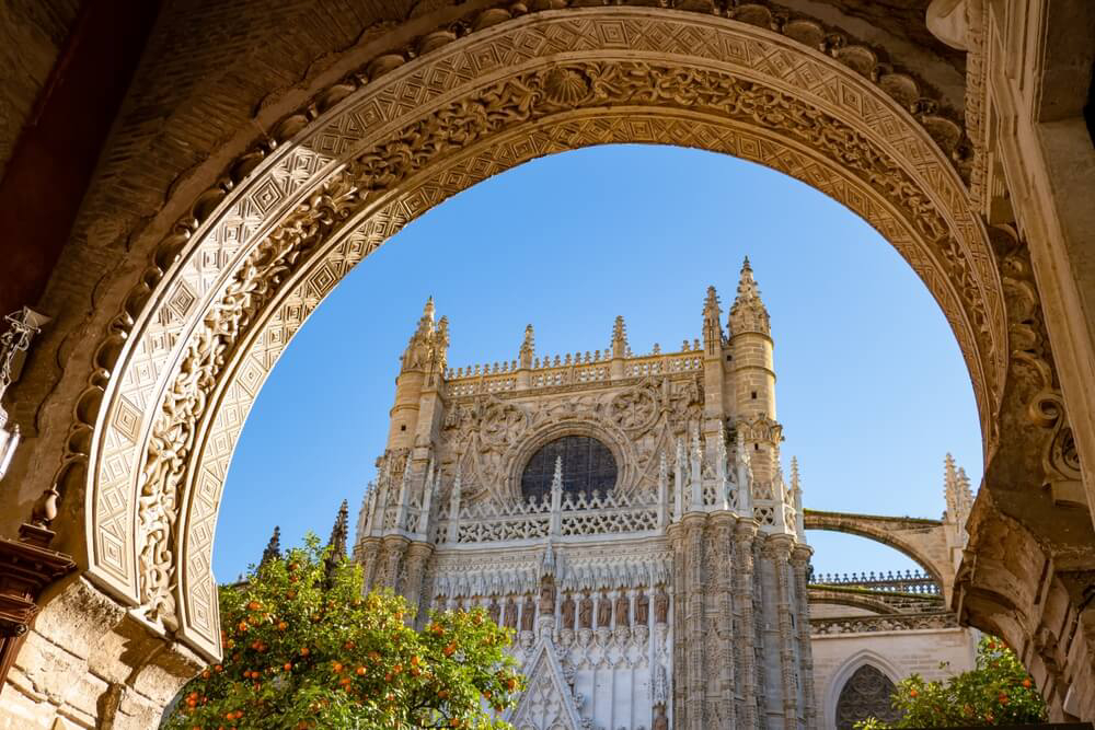 Blick durch einen filigran verzierten Bogen auf die Giralda von Sevilla.