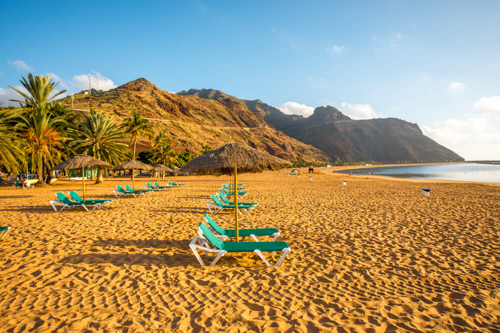 Goldgelber Strand mit Liegen und Palmen.