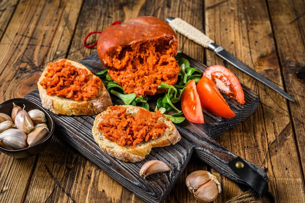 Traditionelle mediterrane Küche: Sobrassada aus Mallorca auf einem Holzbrett mit Brot und Gemüse.