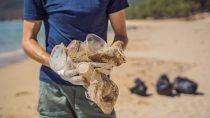 Man in a navy shirt holding dirty plastic cups on the beach 