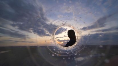 View through the opening of a plastic bottle on a woman that looks out at the horizon