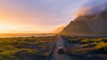 Gravel road at a golden Sunset with Vestrahorn mountain in the background and a car driving the road in Iceland