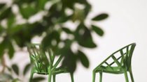 Two green plastic chairs facing each other behind blurred leaves 
