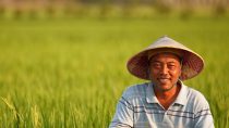 Man sitting in a green long grass field wearing a hat 