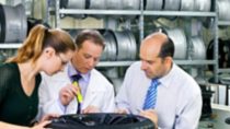 Three people working together inspecting tire rim in a garage 