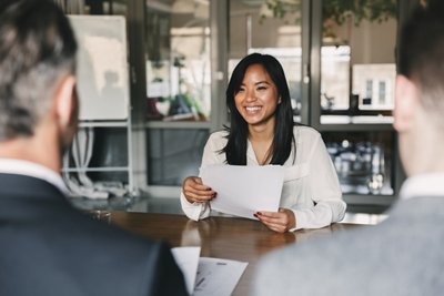 Business, career and placement concept - young asian woman smiling and holding resume, while sitting in front of directors during corporate meeting or job interview