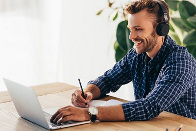 smiling man in headphones taking part in webinar at tabletop with notebook in office