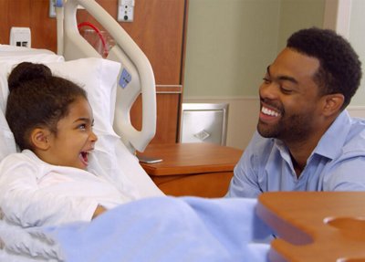 A girl in the hospital smiles at a person from her bed