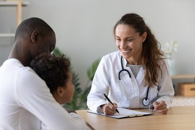 Smiling female doctor listen consult cute african boy make notes in patient card at medical checkup appointment, black dad and child son visit pediatrician talk in clinic, children healthcare concept