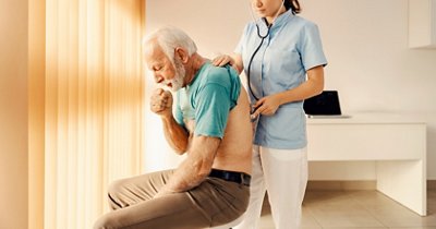 A sick old man coughing and getting medical attention by a female doctor in doctor's office. Heath care, medical support and medical service.
