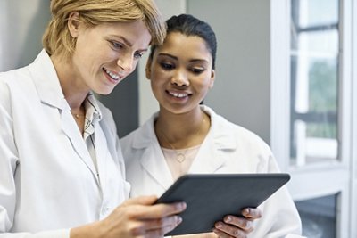 Smiling female scientists discussing over digital tablet. Confident healthcare workers are working in laboratory. Doctors are wearing lab coats.