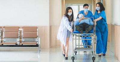 Healthcare professionals transporting a patient on a stretcher through a hospital corridor.