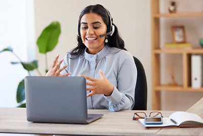 Woman wearing a headset during an online video call, illustrating the VITEK® educational webinars and symposia section of the bioMérieux Product Education Hub.
