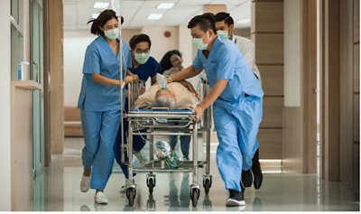 Doctors in blue scrubs and facemasks run through hospital hallway with a patient on a gurney