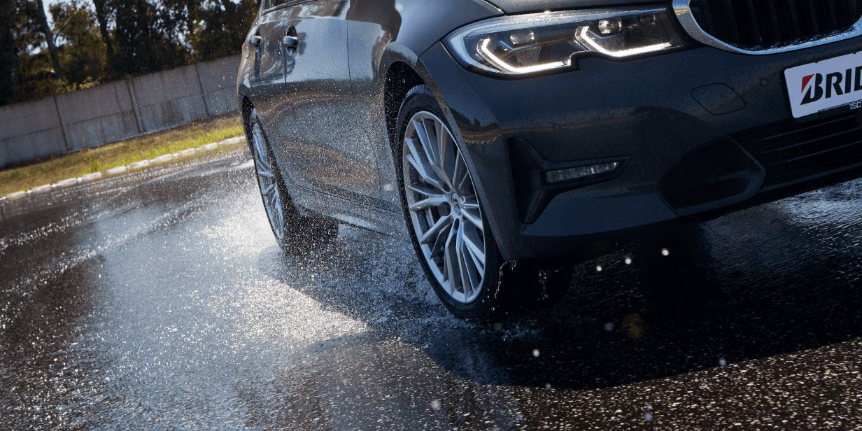 Une vue de face dynamique d’une voiture équipée d’un pneu Turanza en pleine performance sur sol humide.