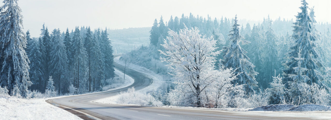 Denna bild visar en motorväg omgiven av ett vackert vinterlandskap, en ideal miljö för Bridgestones vinterdäck för lastbil. 