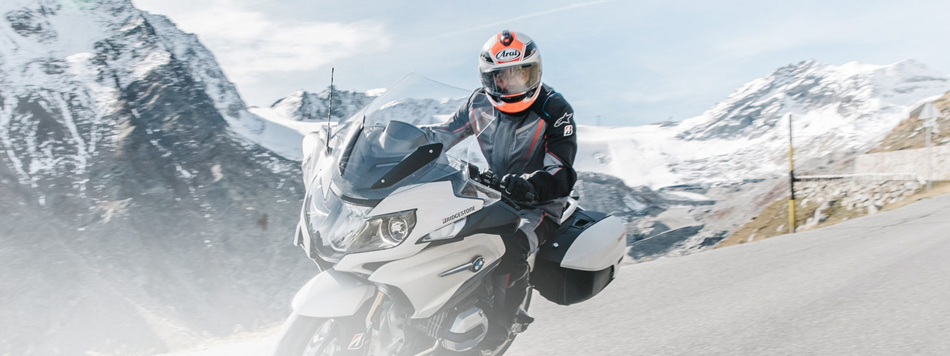 This image shows a motorcyclist riding their motorbike with Bridgestone touring tyres through a scenic road with mountains in the background.