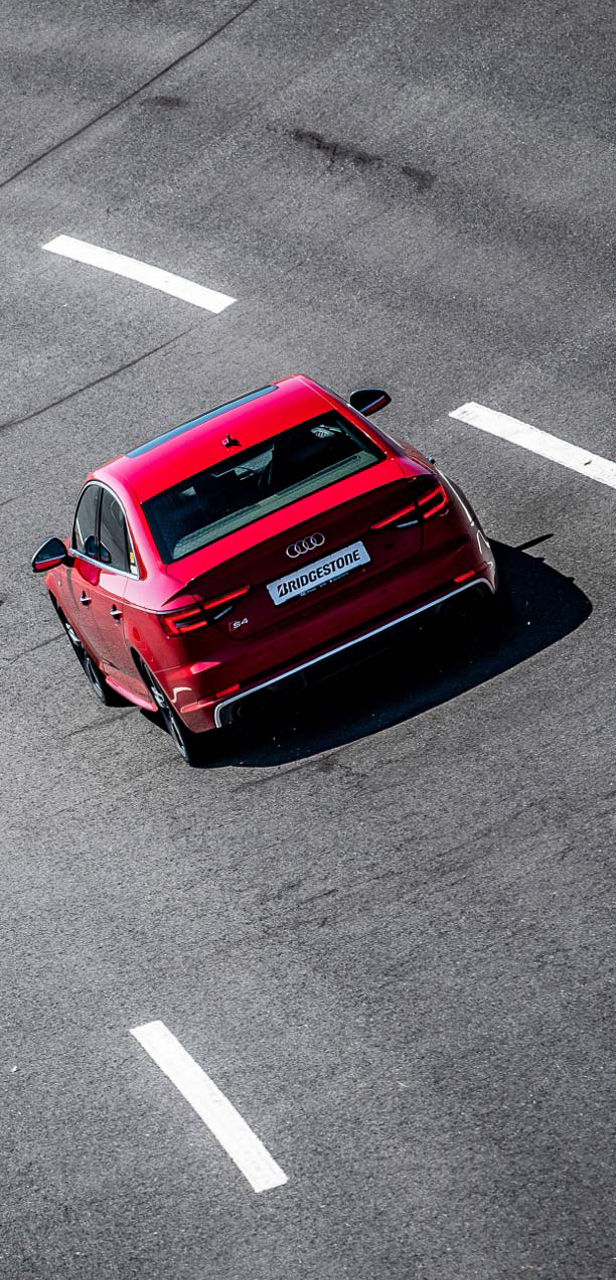 Questa immagine mostra un’Audi S4 rossa equipaggiata con pneumatici Bridgestone Potenza Sport che affronta una curva. 