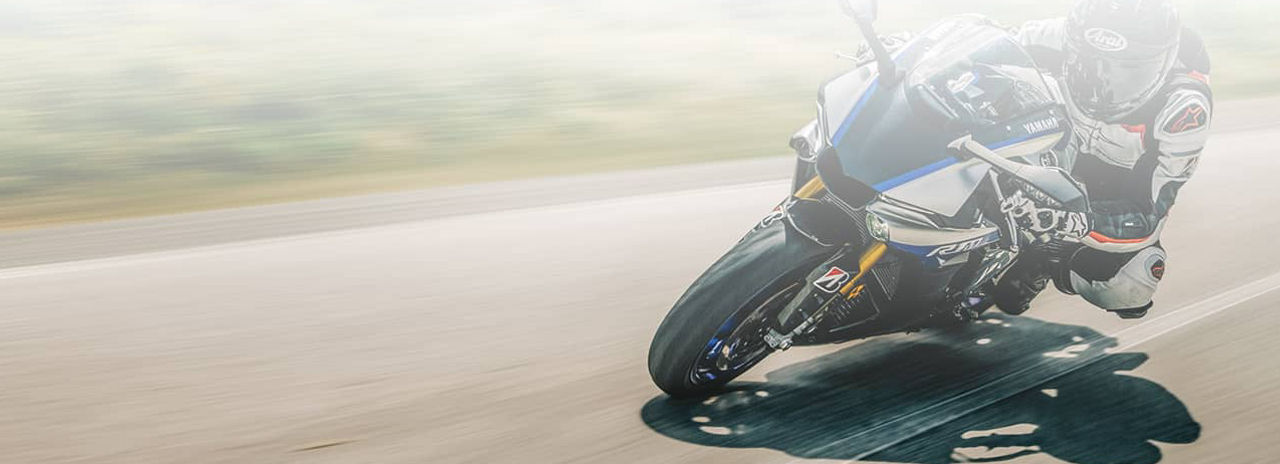 Zdjęcie to przedstawia motocyklistę jadącego po drodze motocyklem na sportowych oponach Bridgestone.