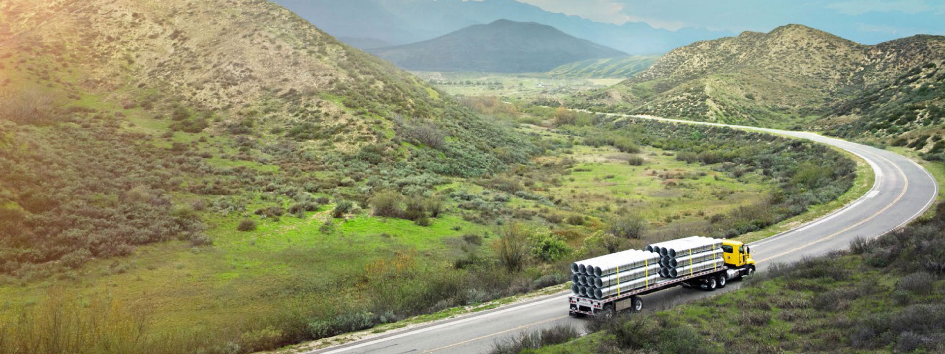A truck on a highway with mountains in the background.