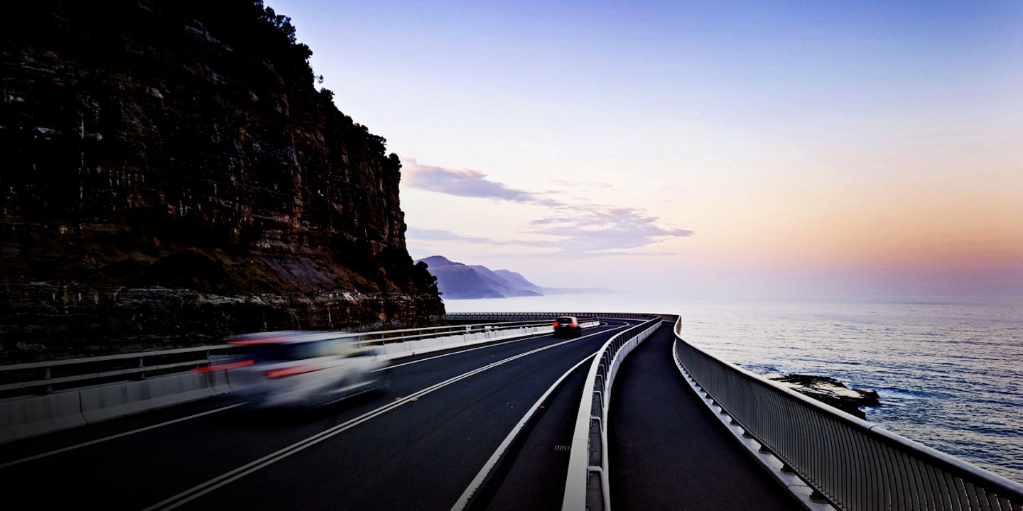 Mit Bridgestone-Reifen ausgestattete Autos fahren auf einer Küstenstraße mit einem Sonnenuntergang im Hintergrund