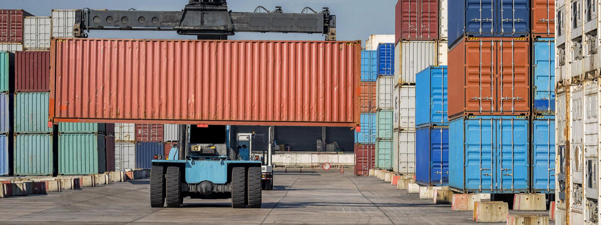 En gaffeltruck utstyrt med terrengdekk fra Bridgestone beveger fraktcontainere over en stor industrihavn