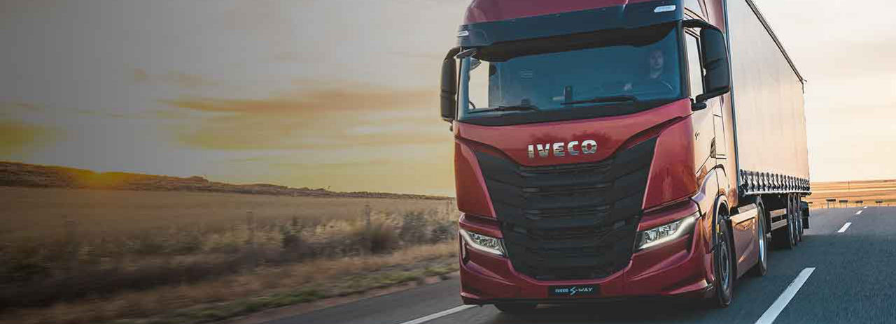 This image shows an Iveco truck travelling down a highway with Bridgestone tyres and a sunset in the background.