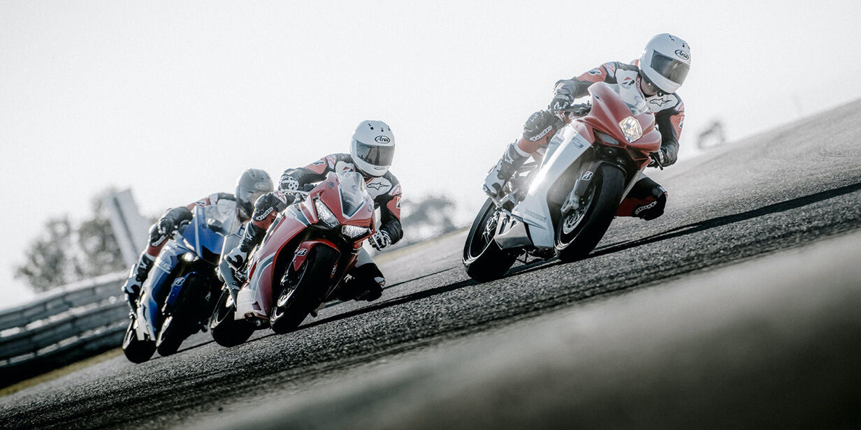 On this image we see three motorcycle racers cornering with Bridgestone tyres on a race track at high speed.